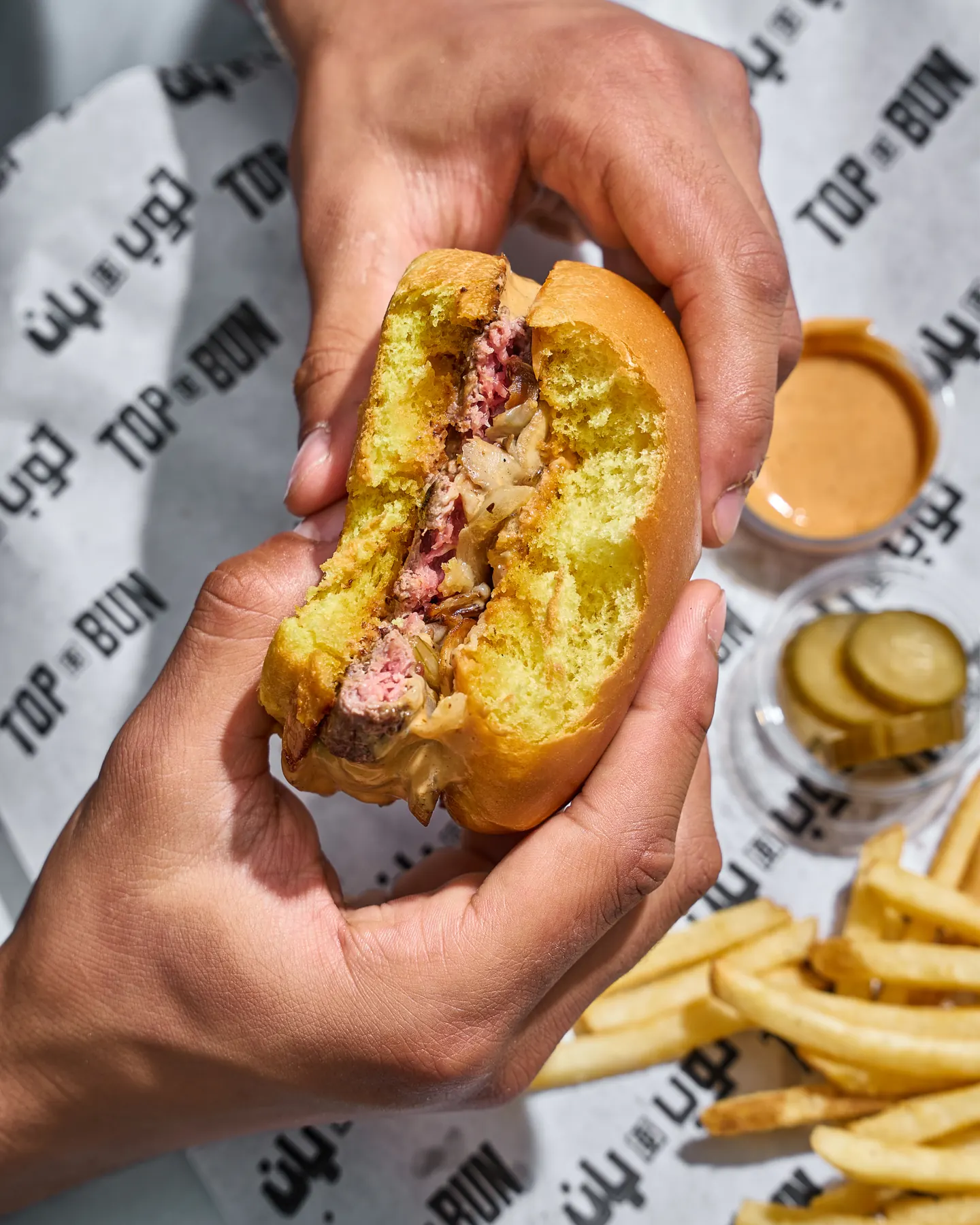 Hands holding a Top Bun burger with house sauce
